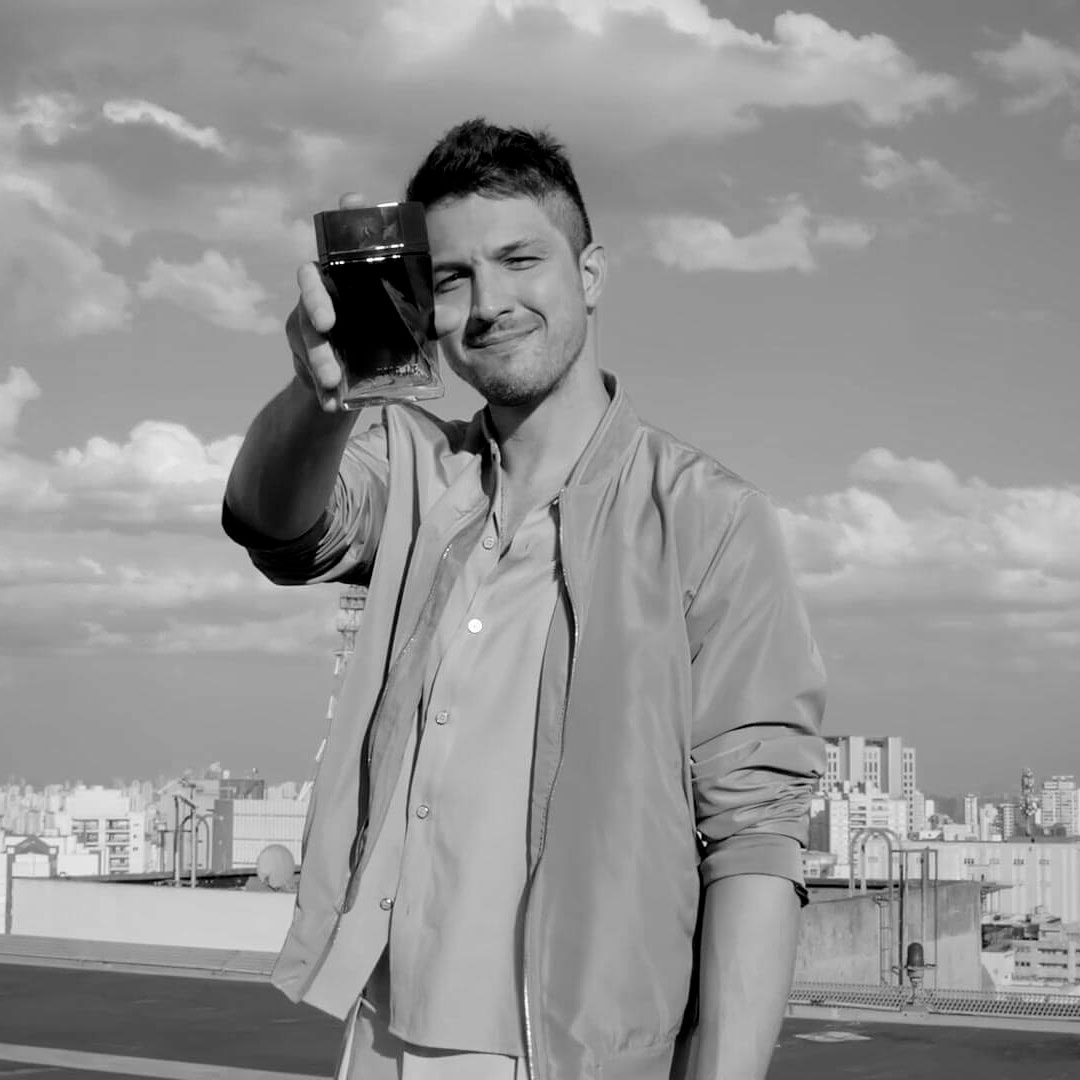 Homem segura frasco de perfume no terraço de um prédio